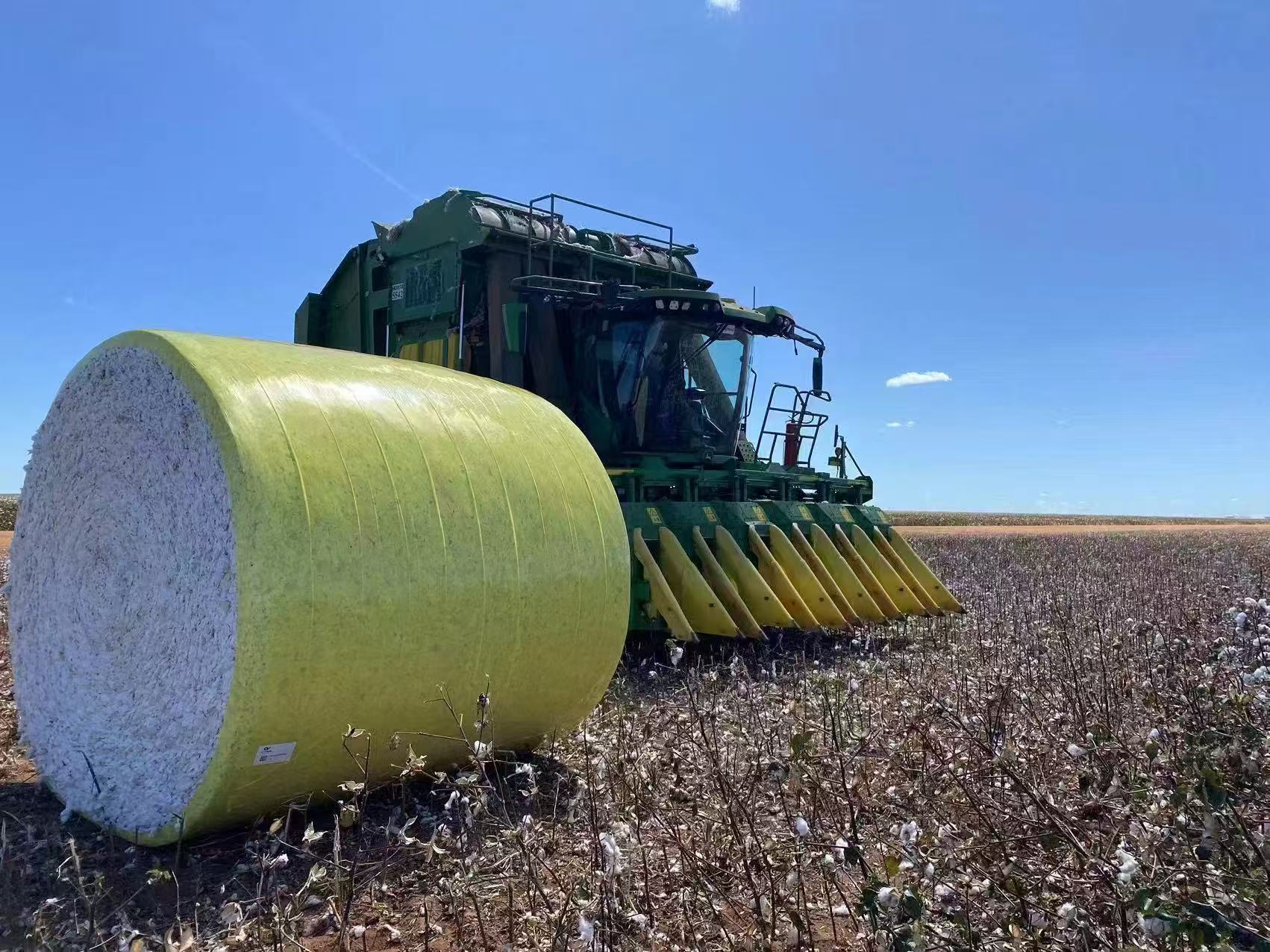 John Deere cotton picker with wrapped cotton bale in field